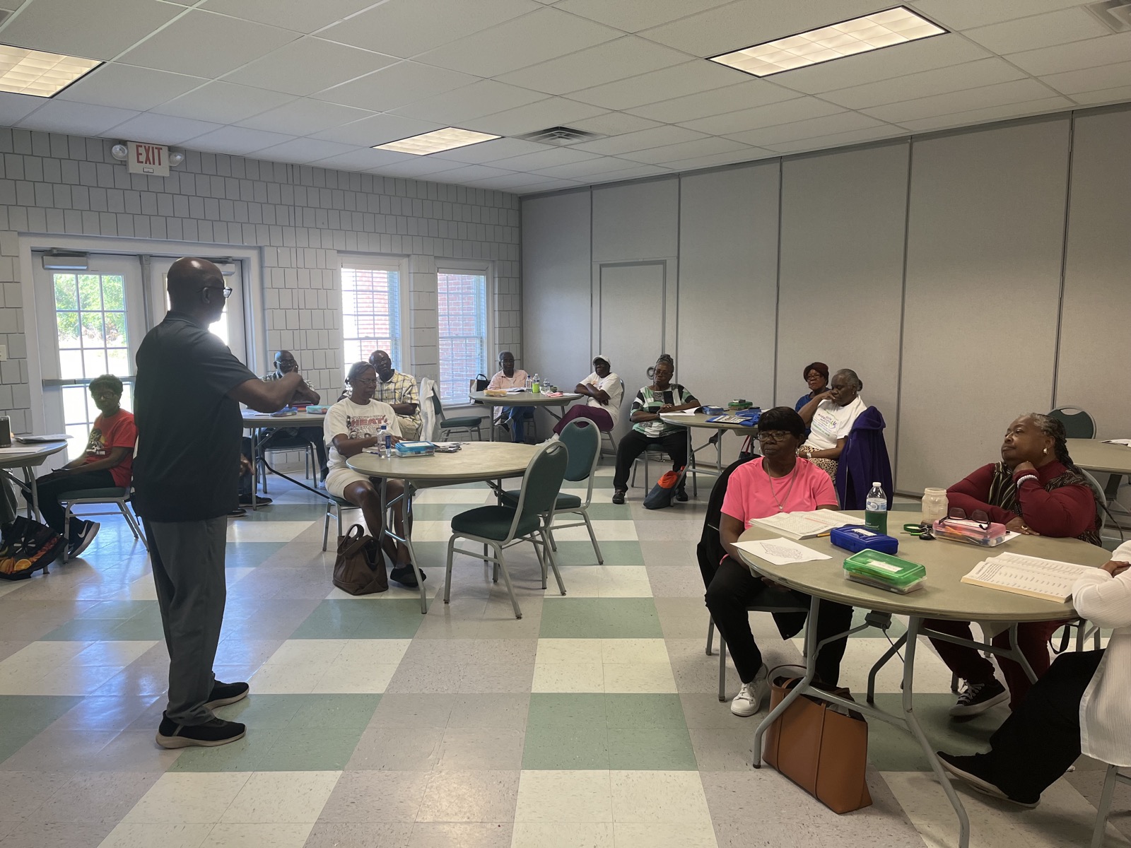 An AccessAbility facilitator leading an emergency preparedness training session for a room of community members seated at tables.