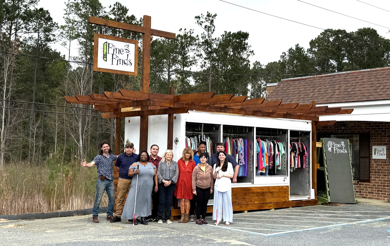 AccessAbility staff and board members at the Fine Finds storefront, racks of clothing visible inside.