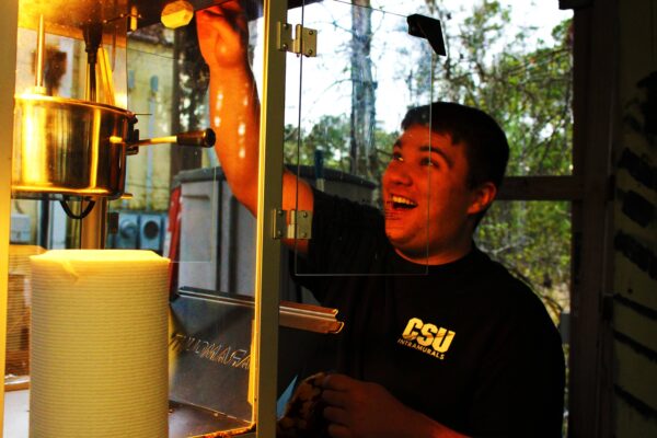 [AccessAbility staff member smiling while making popcorn from a popcorn machine outside]