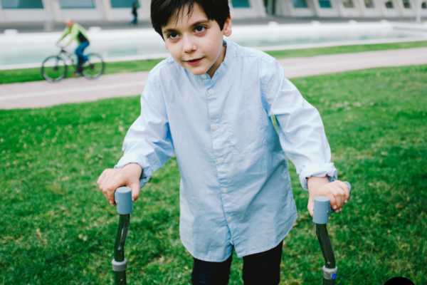 A young child outside using arm crutches.