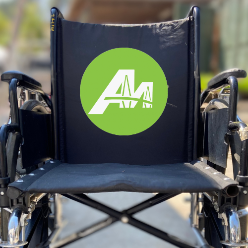 A photo of a wheelchair with the round green and white AccessAbility logo on the backrest of the chair.