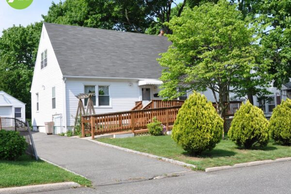 An image of a middle class home with a front yard and handicap accessible ramp leading up to the front door.