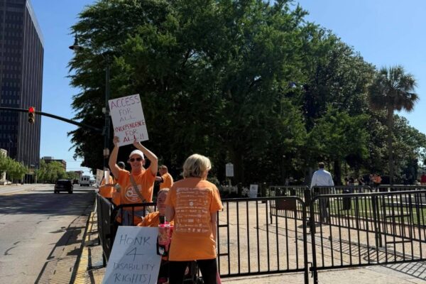 People standing near the street in front of the state capital holding up signs in support of disability rights.