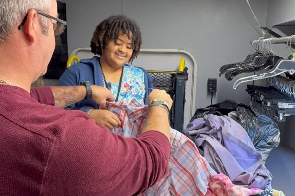 Tony from AccessAbility showing a student how to sort through clothing for the online store.