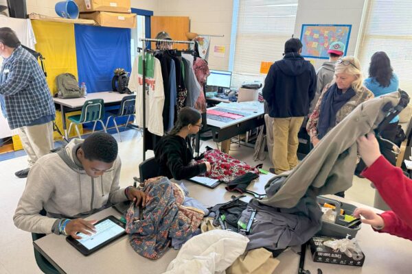 Students and mentors in a classroom working on processing clothing.
