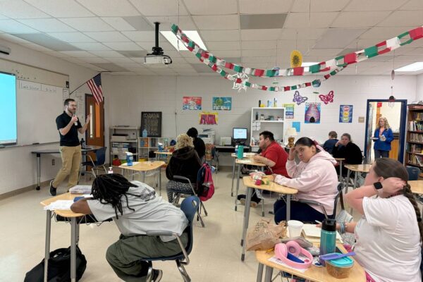 J from AccessAbility teaching in a classroom to a group of students.