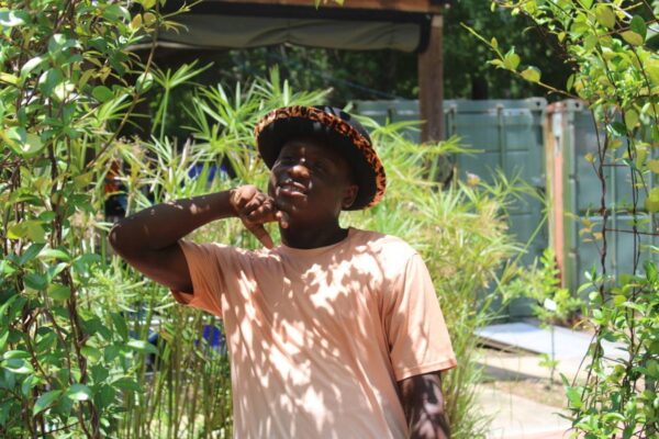 A summer session attendee posing with a leopard print hat in the sensory garden. His hand is raised and positioned under his chin.
