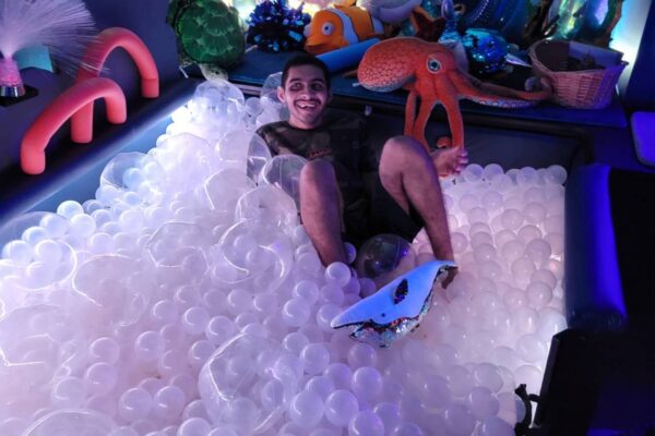 Summer session attendee hanging out in the ball pit in the ocean room at Scotty's Place.