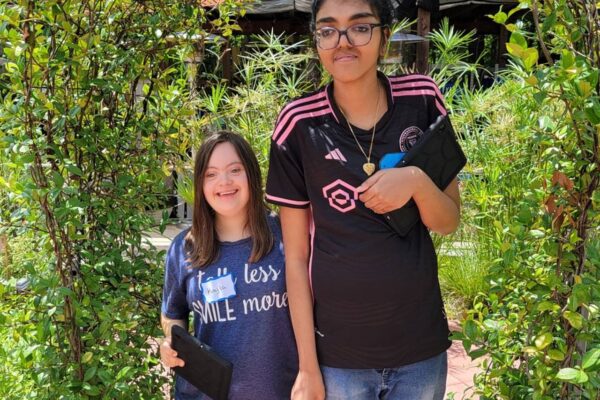 Kayla and Rafia posing under a walkway of flowers in the sensory garden.