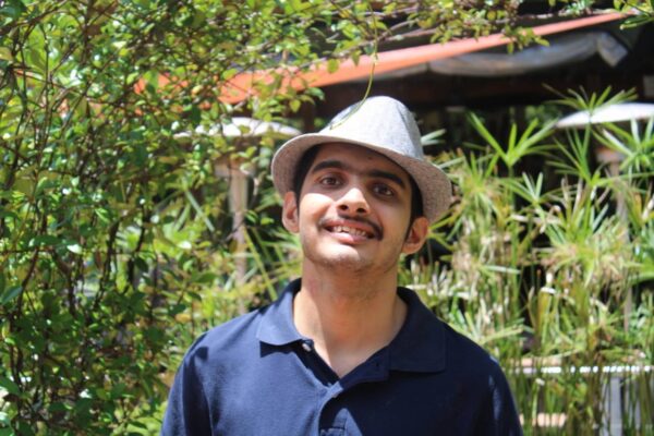 Summer session attendee posing with a hat outside in the sensory garden and smiling.