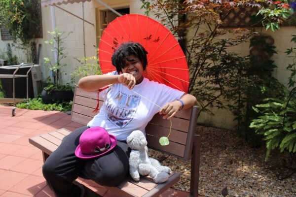A summer session attendee sitting on a bench posing with an umbrella in the sensory garden.