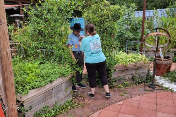Megan from AccessAbility fixing the clothes of a summer session attendee before they pose for a picture in the sensory garden.