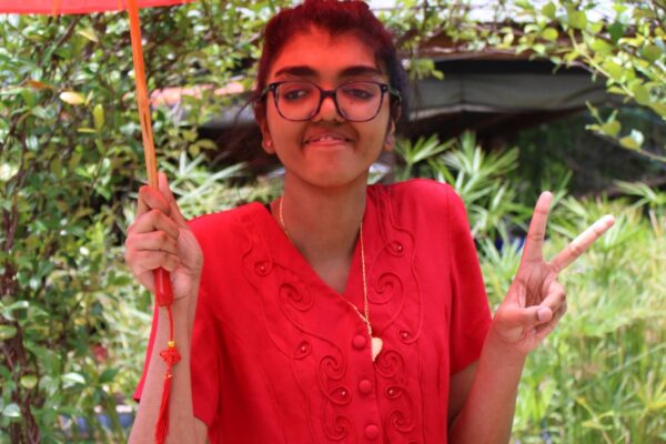 A summer session attendee posing with an umbrella and holding up a peace sign with their hand in the sensory garden.